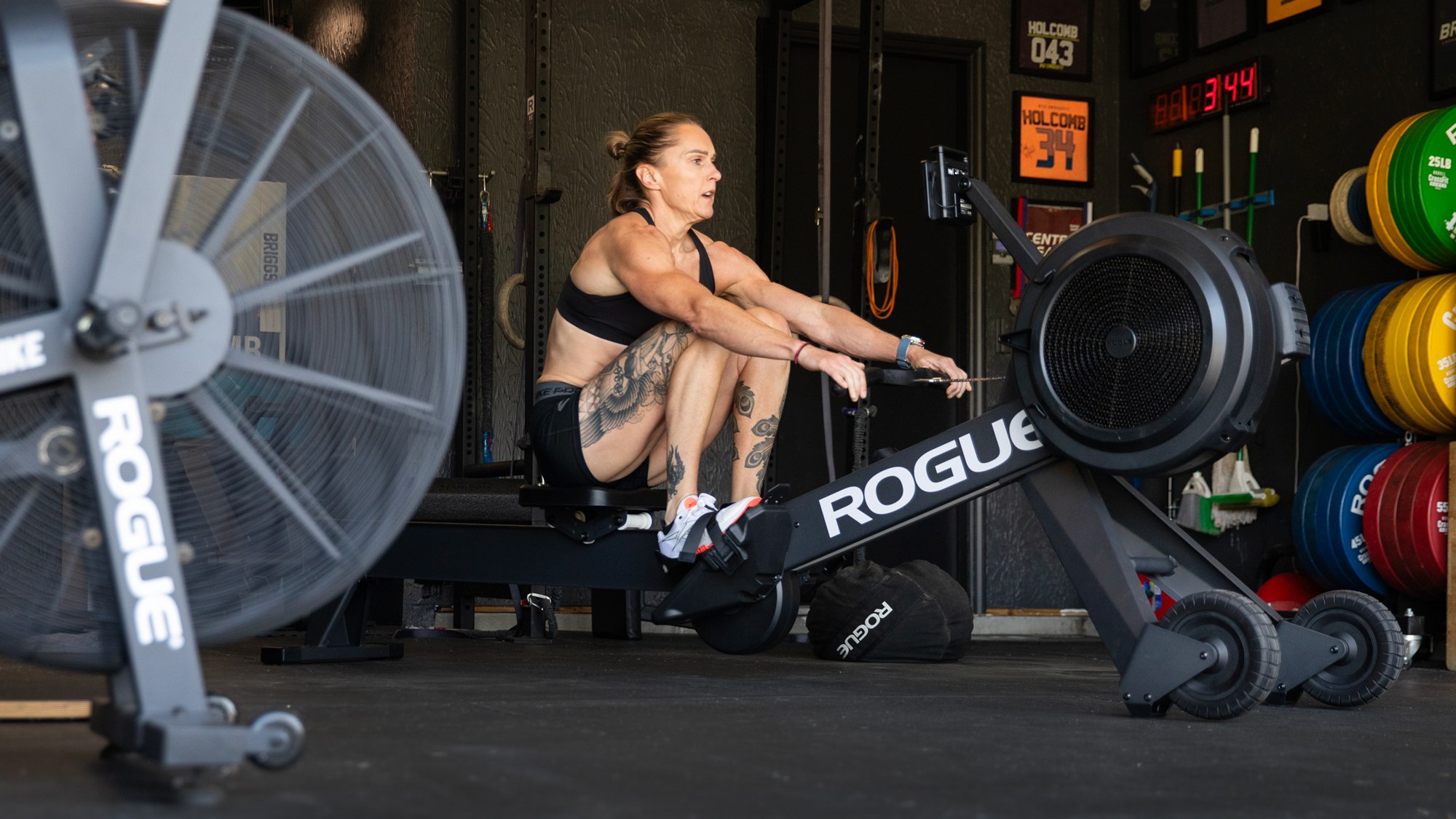 Sam Briggs rema en una Rogue Echo Rower en un gimnasio con discos de colores al fondo